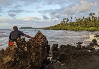 A man sits on a rock and looks across the water