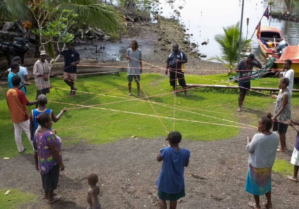 A circle of people playing a game by holding connecting strings