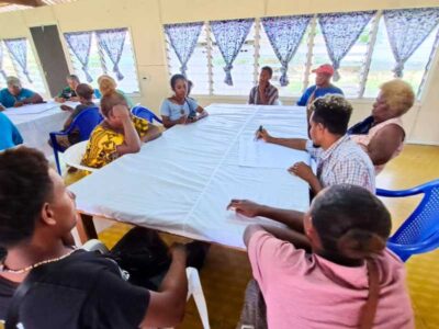 Men and women sit around a square table. One man is taking notes on a large piece of paper.