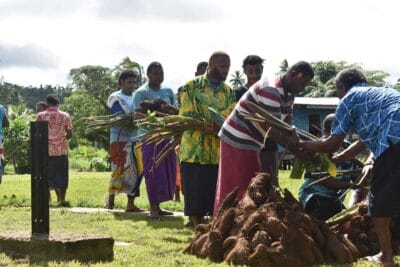 Several men line up holding root crops and other produce