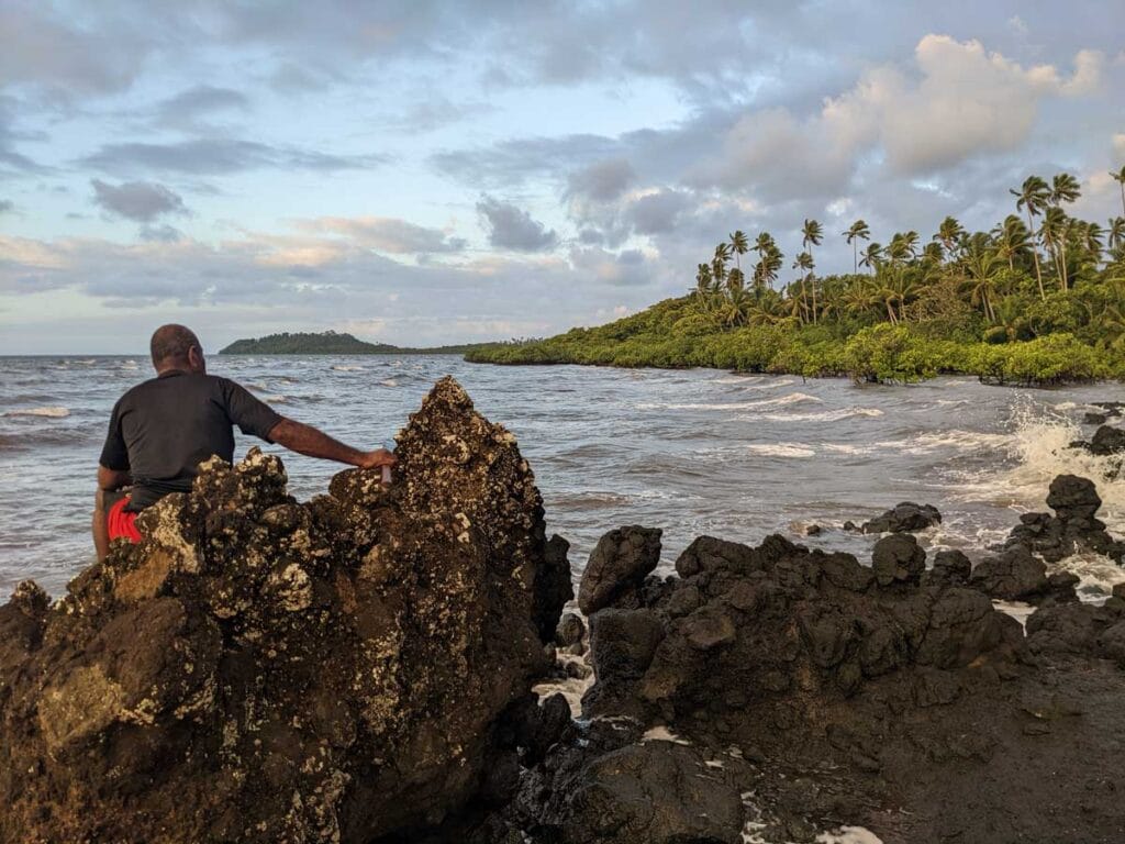 A man sits on a rock and looks across the water