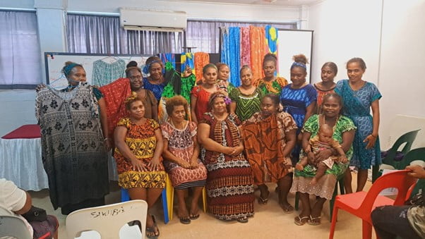 A group of women sitting in front of the clothes they have created