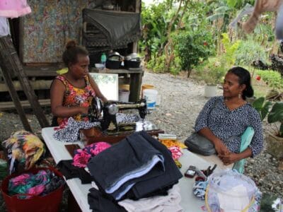 Lilian shares her story with a Live & Learn team member over the large outside table where she sews the clothes for her business